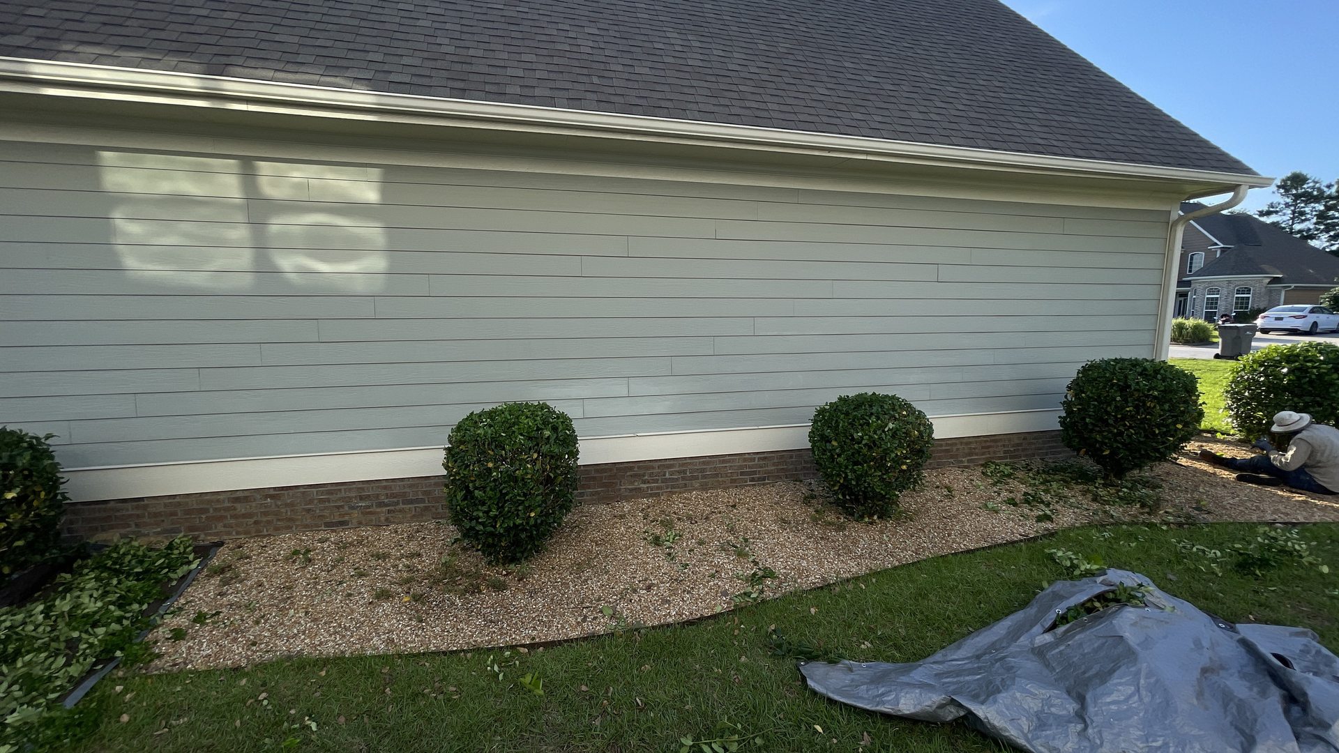 A Transitions crew member trimming shrubs, clippings gathered on a tarp